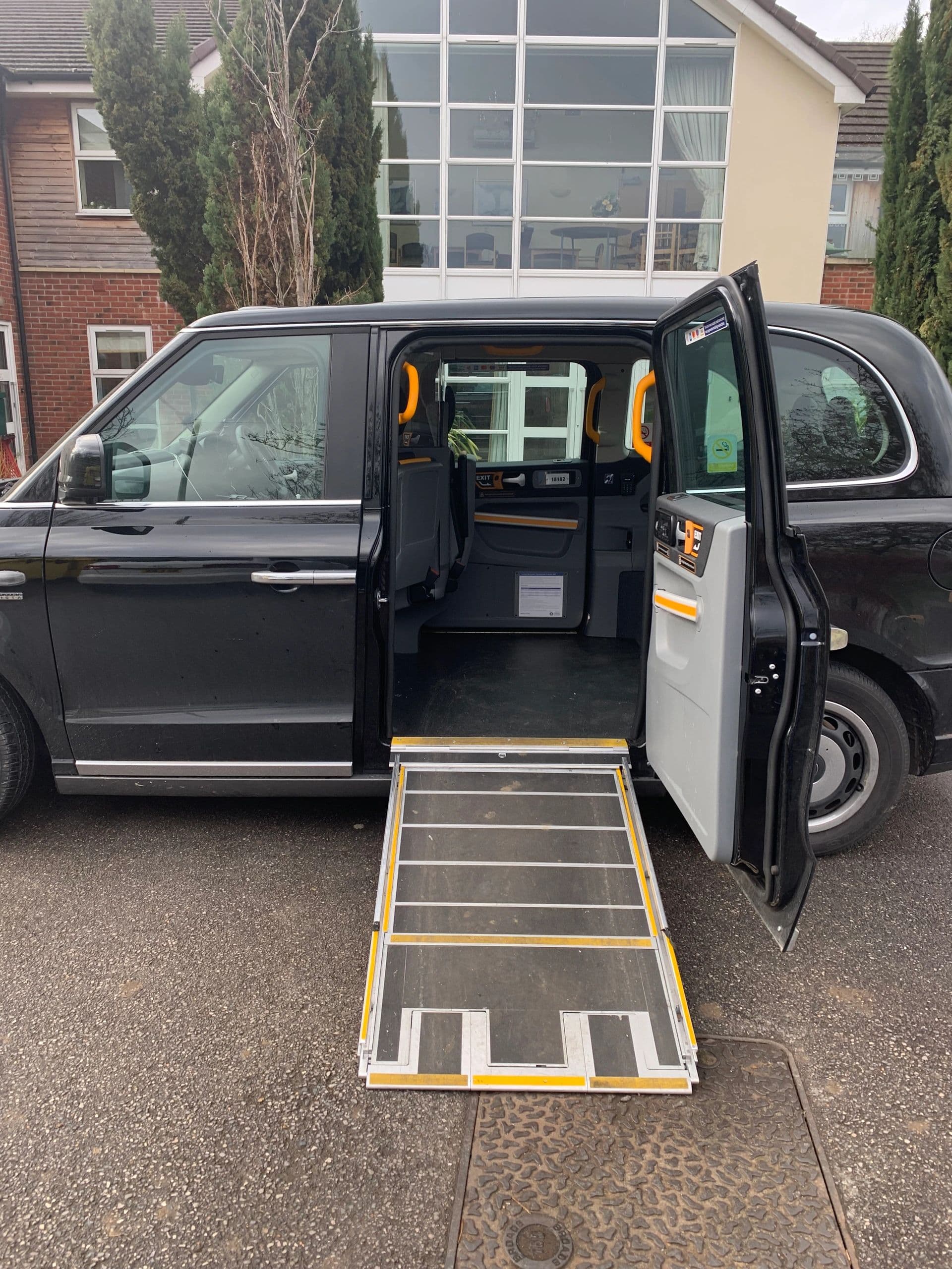 Black taxi with an open door and a wheelchair ramp deployed for accessibility.
