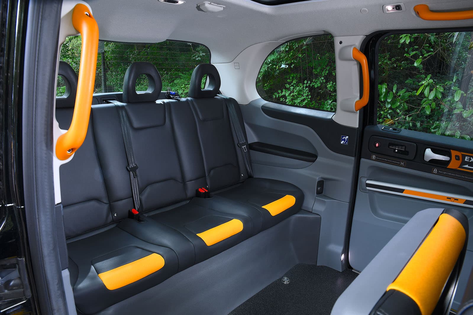 Modern taxi interior with black leather seats, yellow accents, and bright orange grab handles.