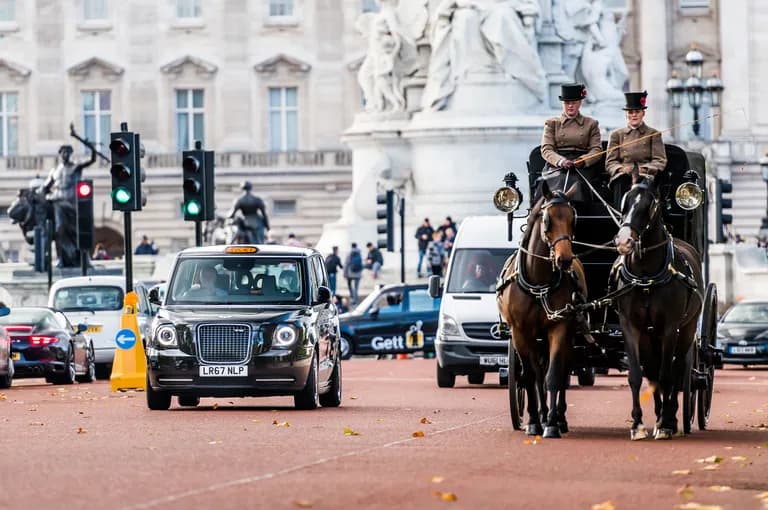 A black London taxi and a horse-drawn carriage drive past the Victoria Memorial.