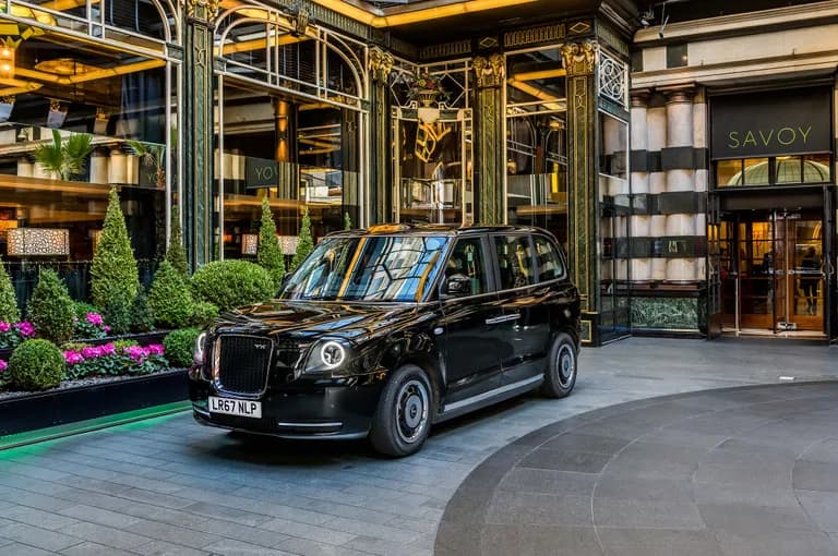 Black London taxi cab parked outside the grand entrance of The Savoy hotel.