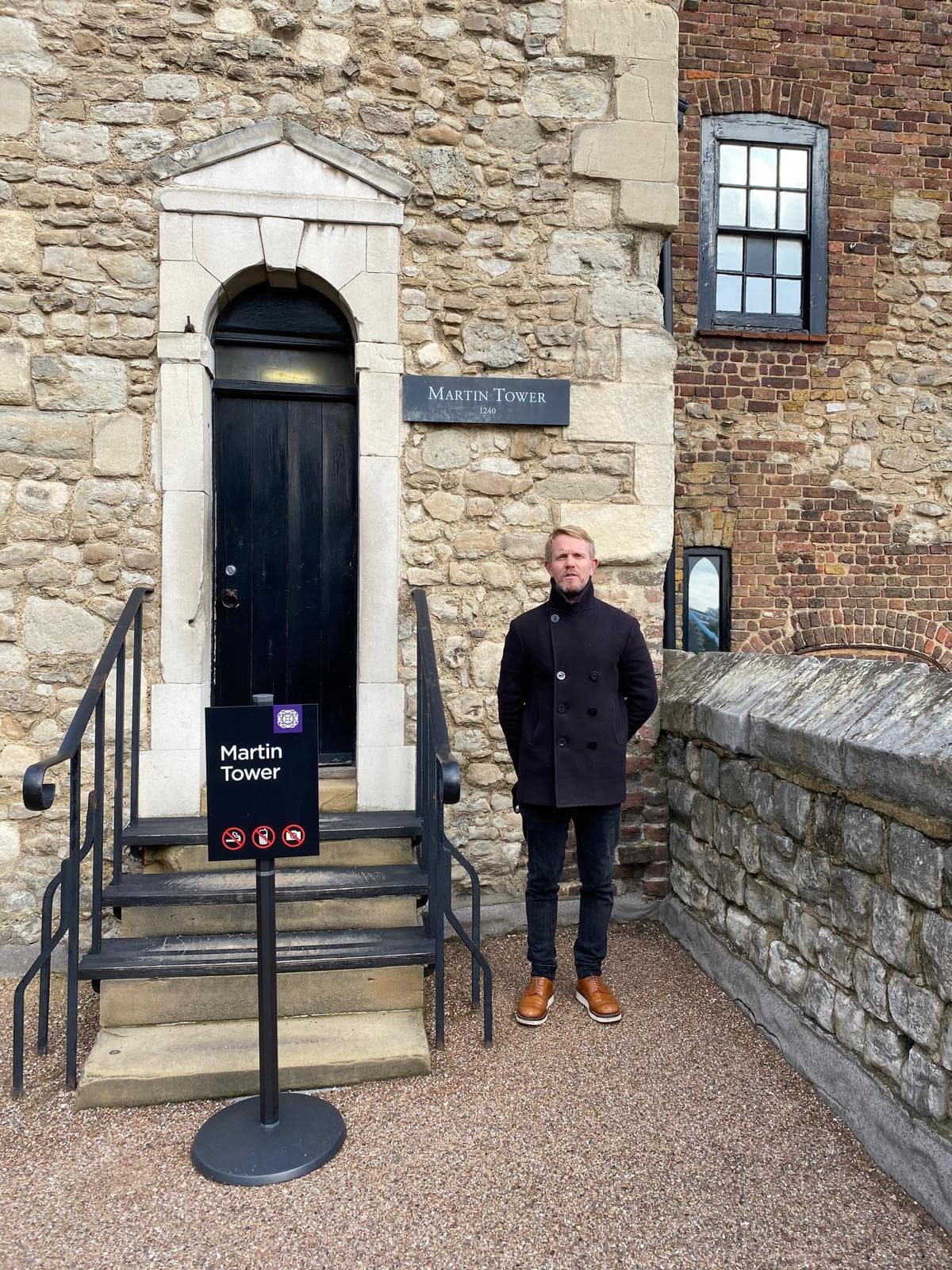 A man in a dark coat stands before the stone entrance of Martin Tower.